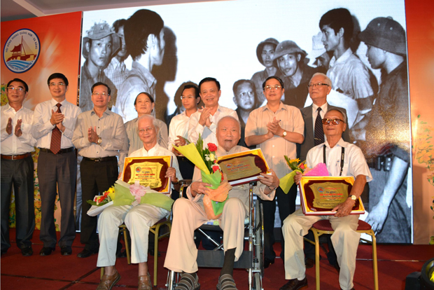 Ông Phạm Kỳ (ngồi ngoài cùng, bên phải) là một trong 3 nhân chứng được lãnh đạo thành phố Đà Nẵng và tỉnh Quảng Nam tuyên dương vì đã có những cống hiến quan trọng cho đất nước. Phía sau là bức ảnh nổi tiếng ông chụp ngày 30-4-1975.