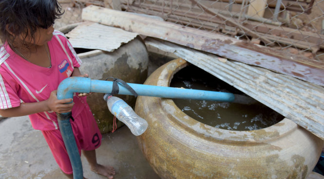 Một bé gái ở Kandal, Campuchia đang chờ bơm nước vào lu chứa - Ảnh: AFP