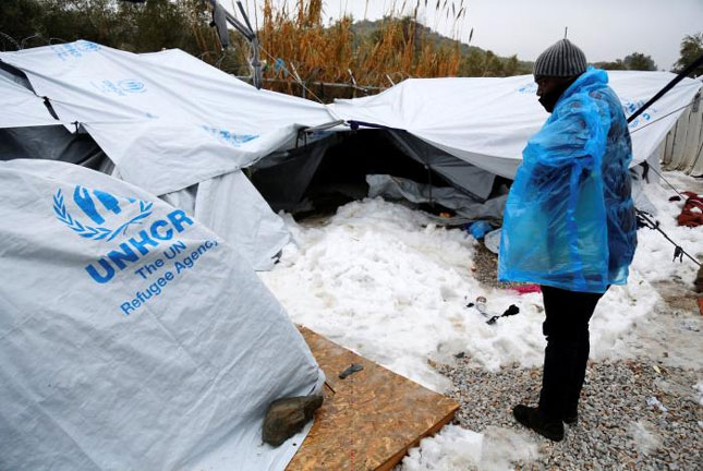 Một người di cư châu Phi  phải mặc thêm áo mưa để chống cái lạnh buốt tại trại tập trung ở Hy Lạp.