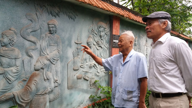 Ông Khoát  (trái) đưa khách tham quan bức tường đắp phù điêu Truyện Kiều.