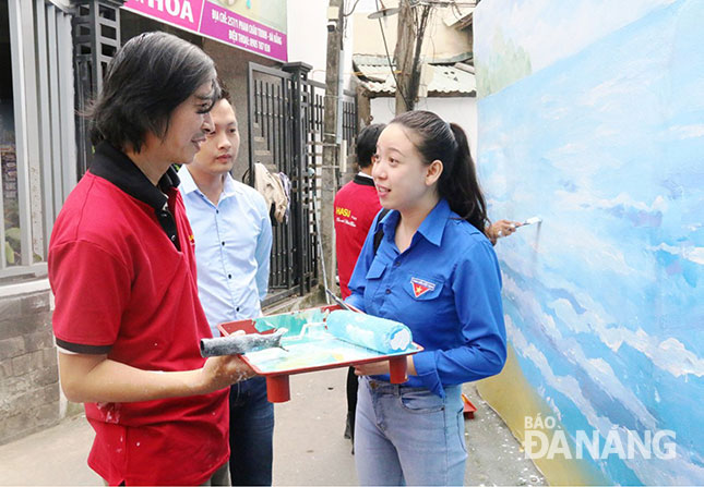 Chị Dương Huỳnh Trang (phải) trao đổi về ý tưởng để các họa sĩ thực hiện những bức tranh tường tại làng bích họa.
