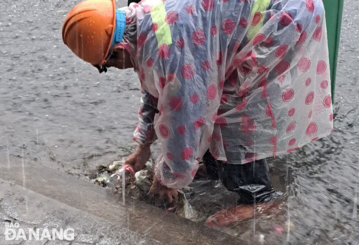 Công nhân Công ty CP Môi trường đô thị Đà Nẵng thu gom rác mắc kẹt tại một cửa thu nước mưa để bảo đảm thoát nước.