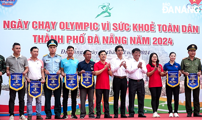 Phó Chủ tịch UBND thành phố Trần Chí Cường (thứ 7, bên trái qua) trao cờ lưu niệm cho các đơn vị tham gia ngày chạy.