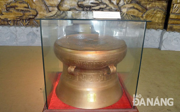 Trước bức phù điêu là chiếc Trống đồng được đúc theo phương pháp thủ công truyền thống Đông Sơn, do các nghệ nhân Lam Kinh, Thanh Hóa thực hiện và là 1 trong 100 chiếc trống đồng được dúc dâng lên Đại lễ 1.000 năm Thăng Long Hà Nội.