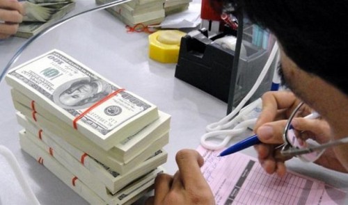 A bank employee works next to stacks of U.S. dollar notes Tuoi Tre