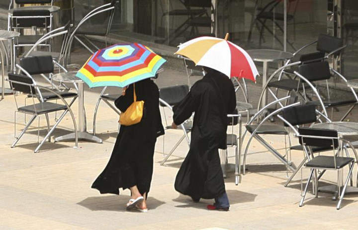   Hai người phụ nữ cầm những chiếc ô sặc sỡ đi qua một quán cà phê ở Riyadh.