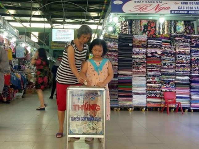 Bé Ngọc và bà đang bỏ tiền ủng hộ vào thùng quyên góp nhân đạo đặt tại chợ Đống Đa.  Ảnh: T.Y