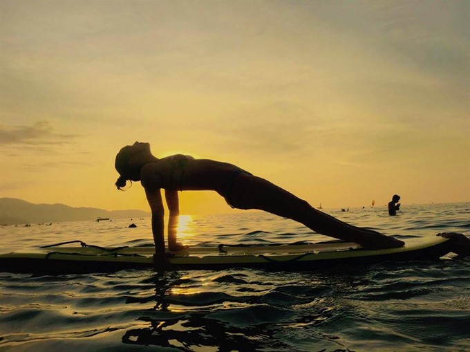 A woman practices yoga on a surfboard in Da Nang