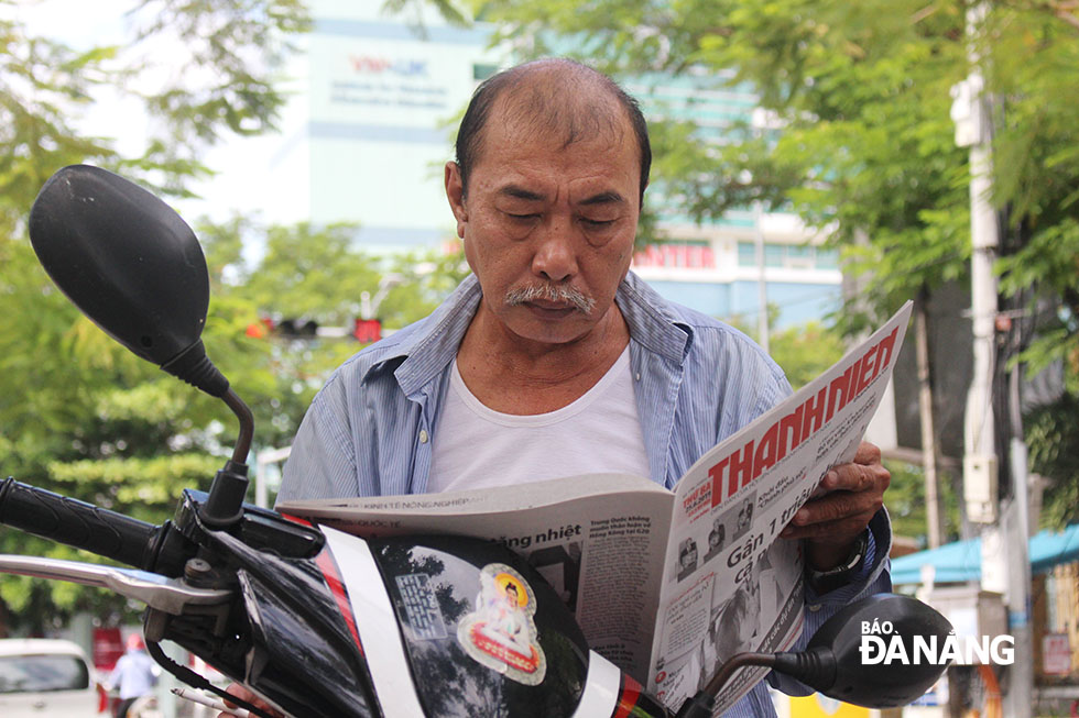 Ông Đô - một phụ huynh đứng đợi con thi ở điểm thi trường THPT Phan Châu Trinh đọc báo để 