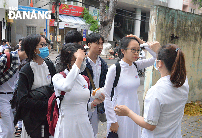 Cán bộ y tế Trường THPT Phan Châu Trinh đo thân nhiệt cho học sinh trước khi các em vào lớp. Ảnh: NGỌC PHÚ