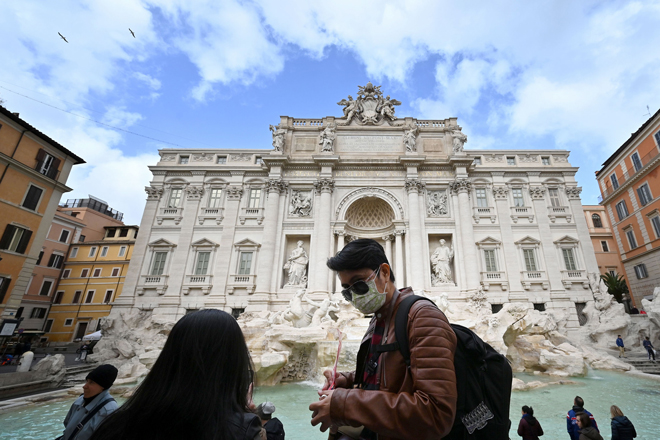 Du khách mang khẩu trang phía trước đài phun nước Trevi tại thành phố Rome của Ý. Người dân Ý trước đây không có thói quen mang khẩu trang khi đi lại trên đường phố. 		              Ảnh: AFP/Getty Images