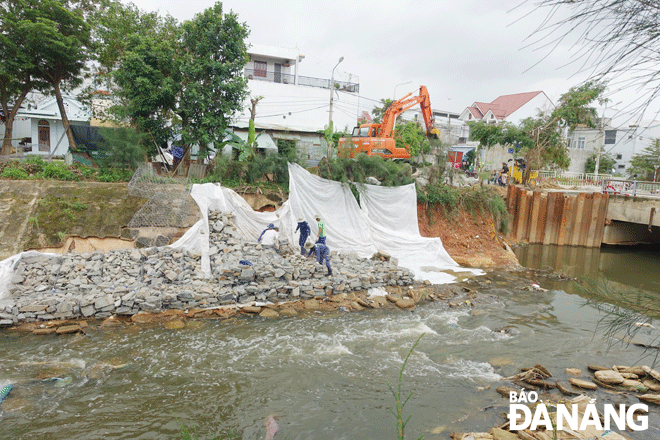 Công ty Thoát nước và xử lý nước thải Đà Nẵng đang huy động phương tiện cơ giới và công nhân khắc phục xói lở bờ kênh thoát nước ở hạ lưu cầu qua đường Nguyễn Xí.  Ảnh: HOÀNG HIỆP