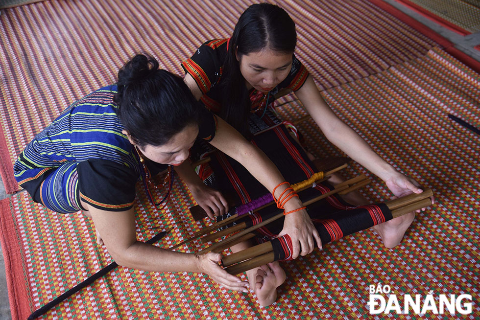 Một nghệ nhân lớn tuổi đang truyền dạy cho cô gái trẻ cách giữ căng khung dệt bằng đôi chân.